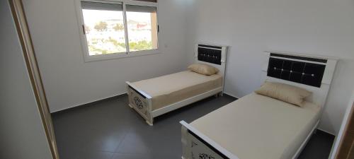 Habitación pequeña con 2 camas y ventana en Logement familial 2 en Selouane