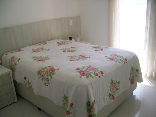 a bed with a white blanket with pink flowers on it at APTO FRENTE TOTAL P/ MAR in Guarujá