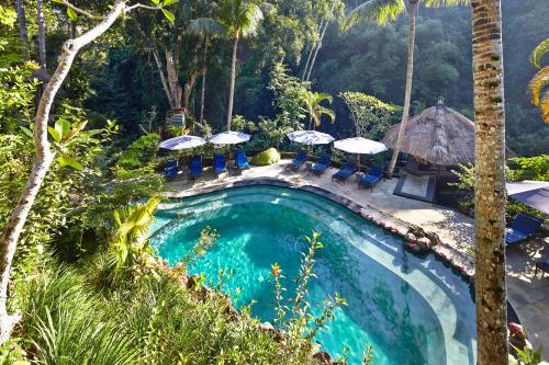 a swimming pool with chairs and umbrellas in a resort at Hotel Tjampuhan Spa in Ubud