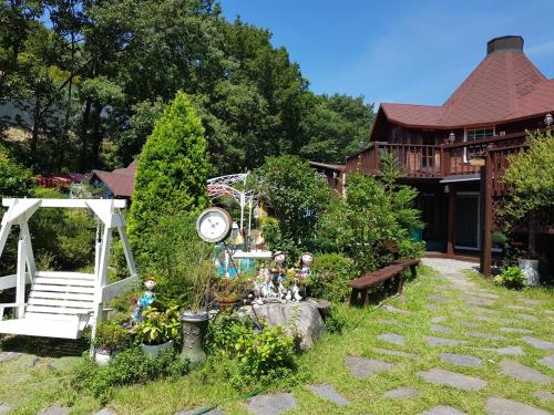 a garden with a clock and a bench and a house at Finland Village Pension in Geoje