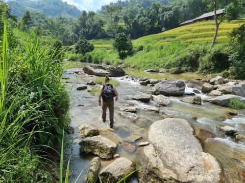 a man walking through a river with rocks at Nậm Lỳ Retreat in Ha Giang
