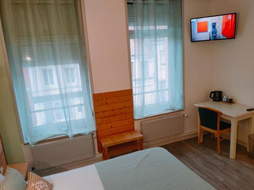 1 dormitorio con 2 ventanas, escritorio y TV en Le Royal Hôtel, en Saint-Pol-sur-Ternoise