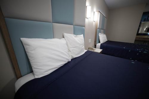 a bed with white pillows and a blue head board at Mid City Inn & Suites Pico Rivera in Pico Rivera
