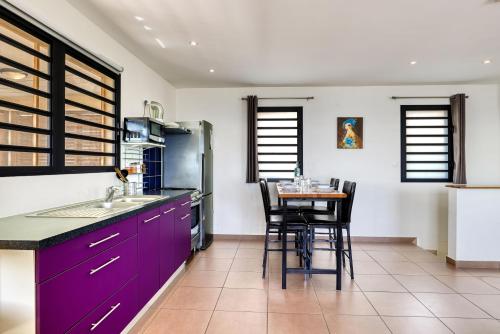 une cuisine avec des placards violets et une table avec des chaises dans l'établissement Bleu Horizon, à Saint-Leu