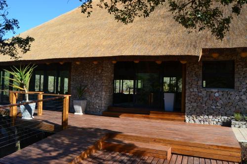 a house with a thatched roof and a wooden deck at Barefoot Addo Elephant Lodge in Addo