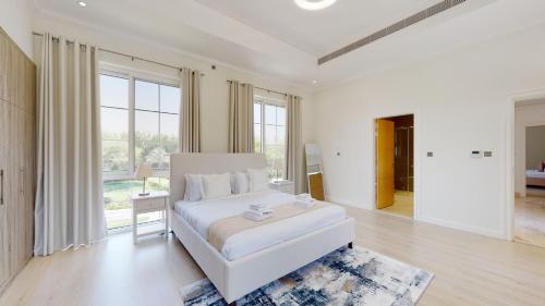 a white bedroom with a bed and a large window at Primestay - Flame Tree Ridge 4BR Villa with Private Pool in Dubai