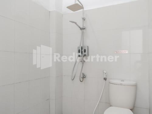 a shower in a white bathroom with a toilet at Khayrizsan Guest House Mitra RedDoorz 