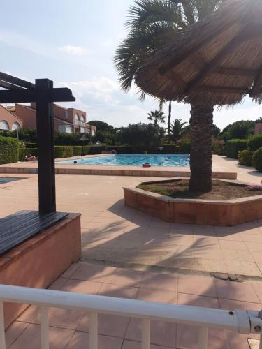 un grand parasol à côté d'une piscine avec un palmier dans l'établissement Studio cabine familial, rez de chaussée,piscine et parking privés, à Palavas-les-Flots
