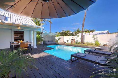 a swimming pool with an umbrella next to a house at VILLA KELOHA - Luxueuse villa créole in Étang-Salé les Bains