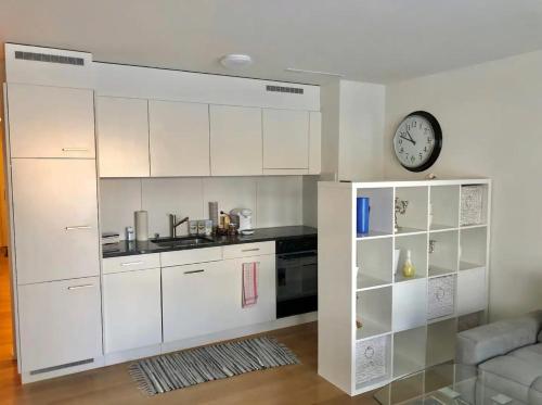 una cocina con armarios blancos y un reloj en la pared en Gemuetliche 2 Zimmer Wohnung mit Gartensitzplatz en Fällanden