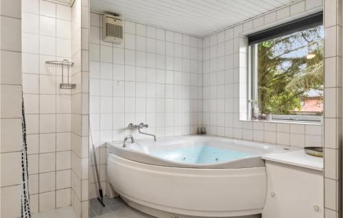 eine Badewanne in einem weiß gefliesten Bad mit einem Fenster in der Unterkunft Patalavaca in Blåvand