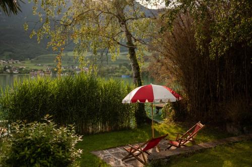 two chairs and a red and white umbrella in the grass at Leuchtenburg am See in Caldaro