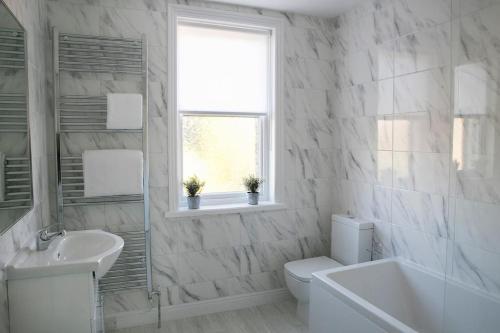 a white bathroom with a sink and a toilet and a window at Valley Road, Fabulous 4 bedroom house in Harrogate