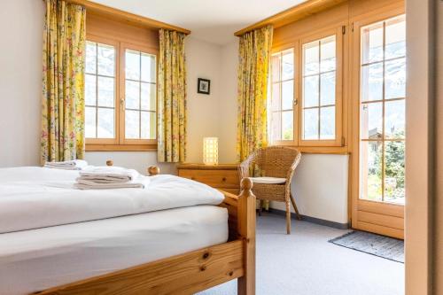 a bedroom with two beds and a chair and windows at Apartment Hori - GRIWA RENT AG in Grindelwald