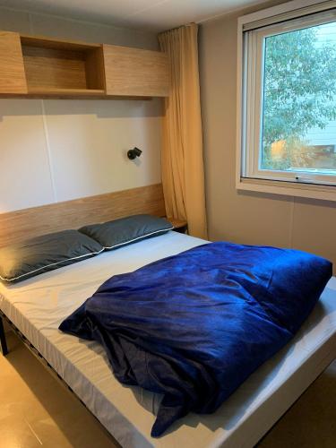 - un lit avec une couverture bleue devant une fenêtre dans l'établissement Mobil Home La Palmyre Camping Bonne Anse 4 étoiles, aux Mathes