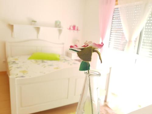 a glass vase with a flower in front of a bed at Casa de Praia acolhedora/ Cosy beach house in Marinha das Ondas