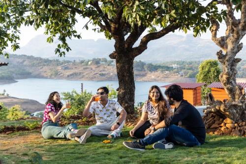 un grupo de personas sentadas en la hierba bajo un árbol en The Hosteller Bhandardara, en Bhandardara