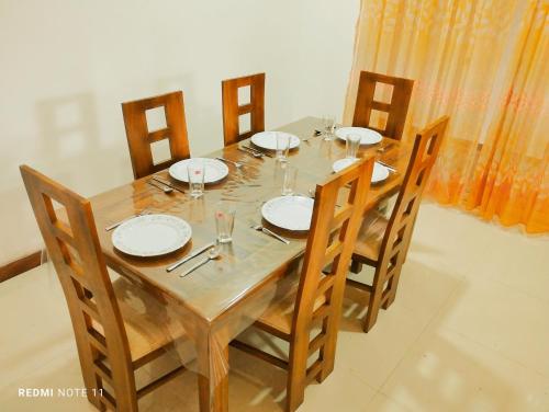 einem Holztisch mit Stühlen, Tellern und Gläsern darauf in der Unterkunft New White House in Colombo