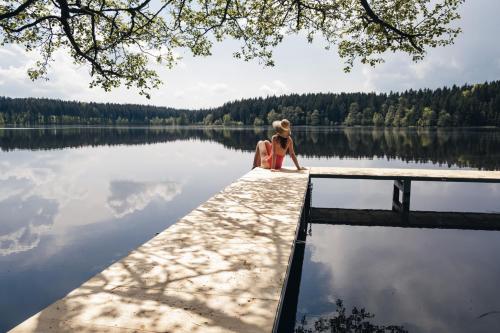 una mujer sentada en un muelle cerca de un lago en Hotel Medlov en Nové Město na Moravě