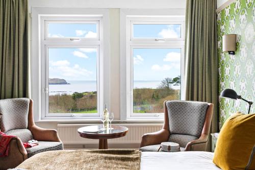 a hotel room with two chairs and a bed and two windows at Thurlestone Hotel in Thurlestone