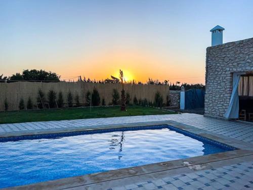 einen Pool in einem Garten mit Sonnenuntergang im Hintergrund in der Unterkunft Oasis Villa Essaouira in Essaouira