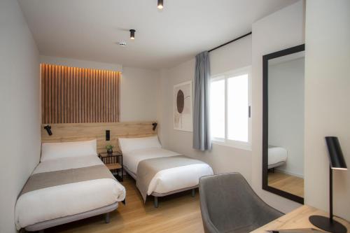 una camera con due letti, una sedia e uno specchio di Aila II Hotel Boutique by SingularStays - Digital Access a Burjassot