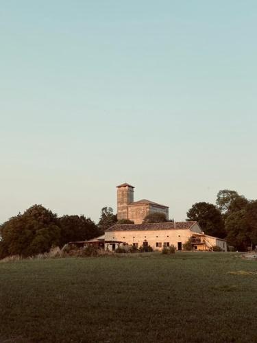 un bâtiment avec une tour au-dessus d'un champ dans l'établissement Maison Drôles d'Oiseaux, à Plieux