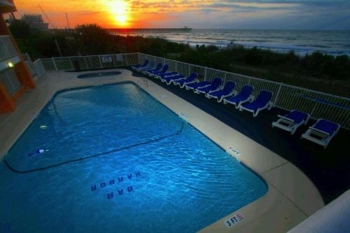 uma piscina com cadeiras e o oceano ao pôr do sol em Bar Harbor em Myrtle Beach