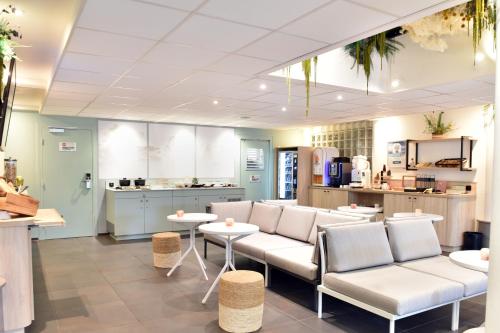 a restaurant with white chairs and tables and a kitchen at Hôtel Kyriad La Rochelle Centre Ville in La Rochelle