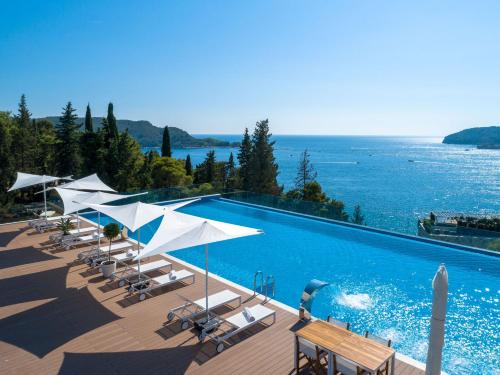 a swimming pool with chairs and umbrellas and the ocean at Hotel Harmonia by Dukley in Budva