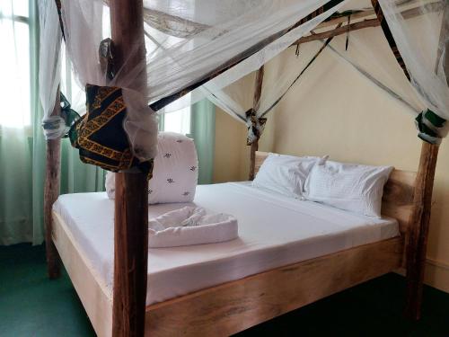 um quarto com uma cama de dossel com lençóis e almofadas brancos em Hill View Garden Hotel em Moshi