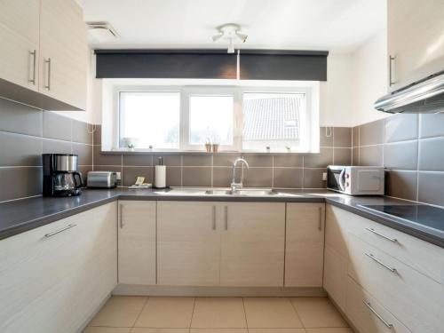 uma cozinha com armários brancos, um lavatório e uma janela em Apartment Caddy by Interhome em De Haan