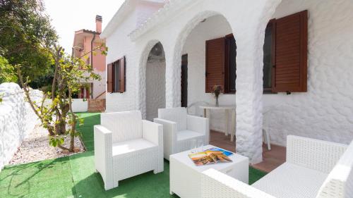 a patio with white chairs and a table at Welcomely - Sandy House in Putzu Idu