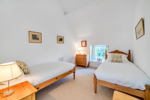 two beds in a room with a lamp and a table at Lower Farm Cottage 