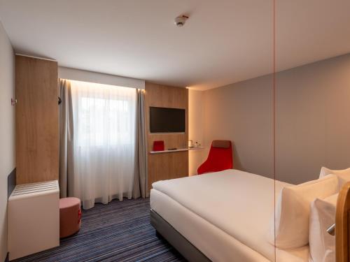 a hotel room with a white bed and a red chair at Holiday Inn Express - Hamburg South A7-AS42 by IHG in Egestorf