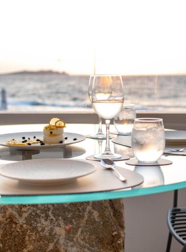 a table with a plate of food and wine glasses at Mykonos Bay Resort & Villas in Mýkonos City