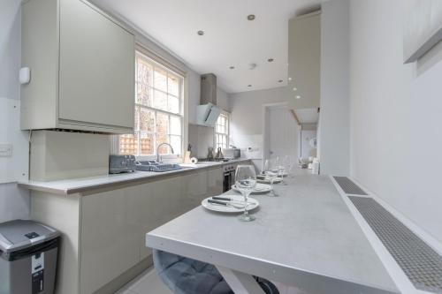 a white kitchen with a long table with wine glasses on it at Charming Character House London in London