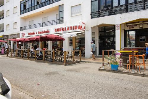 a restaurant with tables and umbrellas on a city street at Lindo T2 com vista mar in Quarteira