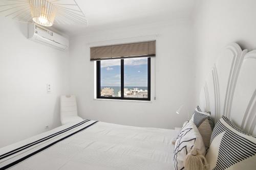 a white bedroom with a bed and a window at Lindo T2 com vista mar in Quarteira