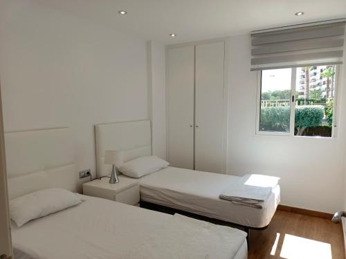 Duas camas num quarto branco com uma janela em Le Panorama Appartement em El Campello