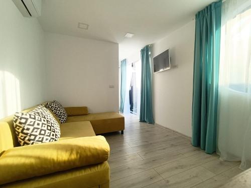 sala de estar con sofá amarillo y cortinas azules en Tiny Village Mamaia Nord - House 2, en Mamaia Nord – Năvodari