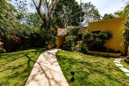 a garden with a yellow house and a sidewalk at Hotel Rancho Encantado in Bacalar