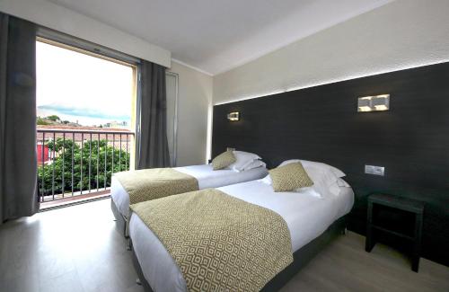 two beds in a hotel room with a large window at Le Cheval Blanc in Arles