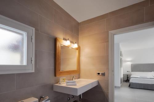 a bathroom with a sink and a mirror and a bed at Alojamientos Turísticos Cardona - Estudio Doble Superior in Es Pujols