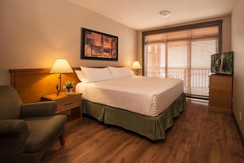 a bedroom with a bed and a chair and a television at Palliser Lodge — Bellstar Hotels & Resorts in Golden