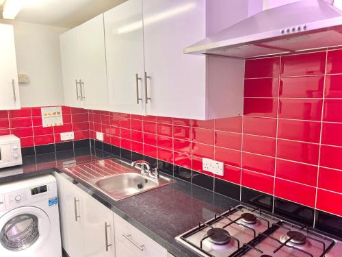 a red tiled kitchen with a sink and a washing machine at White chapel Holiday 2 Bedroom Apartment in London