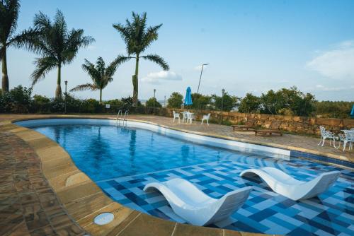 a swimming pool with white chairs and palm trees at Hotel Finca Buenos Aires Barichara in Barichara
