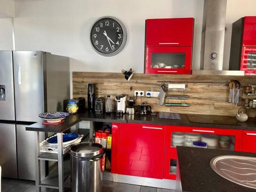 une cuisine avec des placards rouges et une horloge murale dans l'établissement kerwatt, à Cabourg