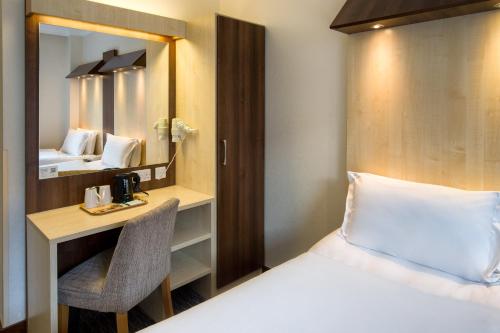 a bedroom with a bed and a desk and a mirror at Royal National Hotel in London