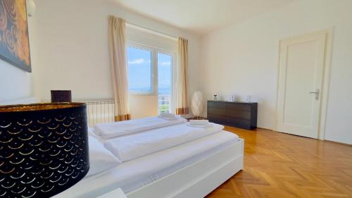 a white bedroom with a bed and a large window at Apartment Reful in Kraljevica